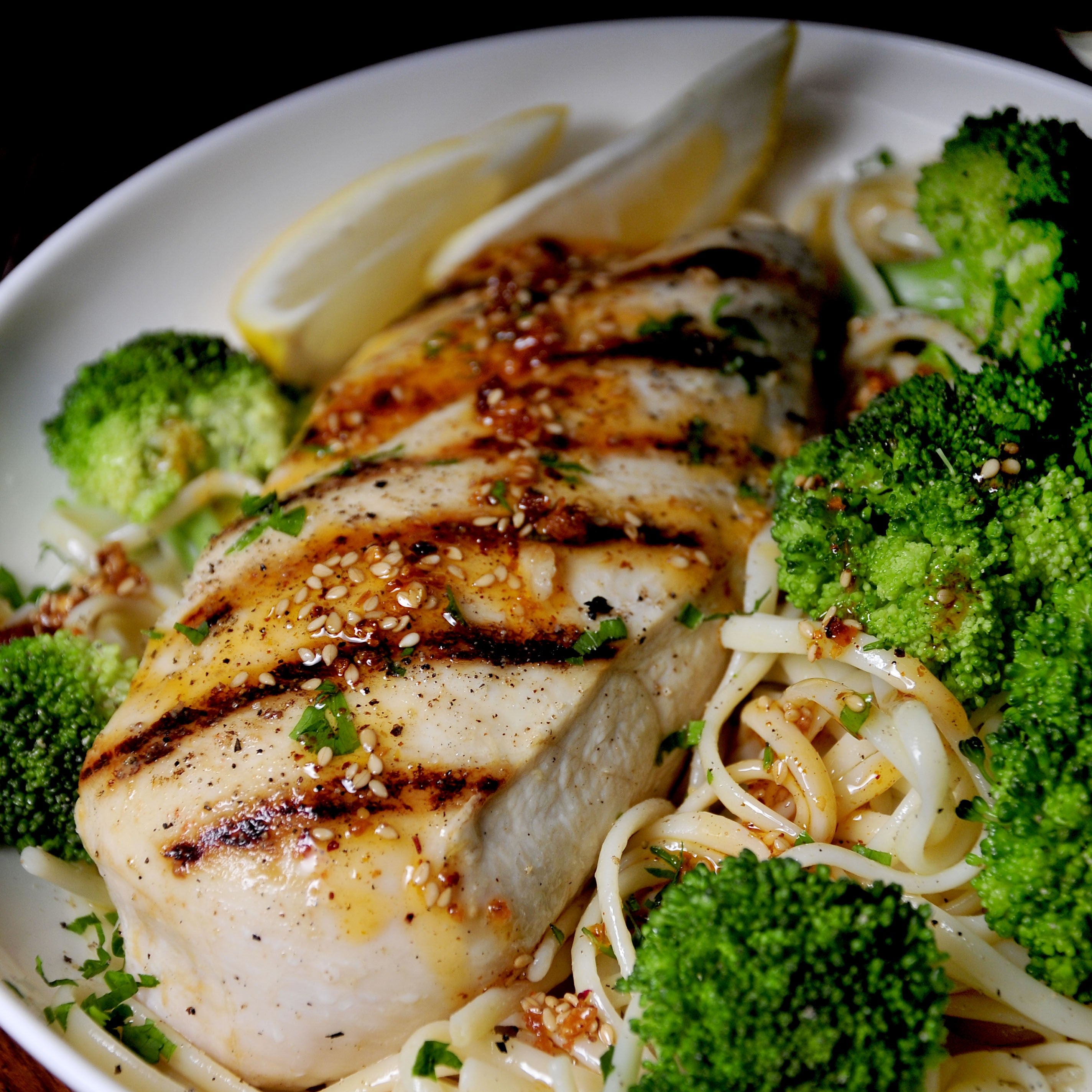 Ruby Crunch chili crisp spooned onto grilled chicken breast, steamed broccoli, and pasta garnished with fresh lemon wedges