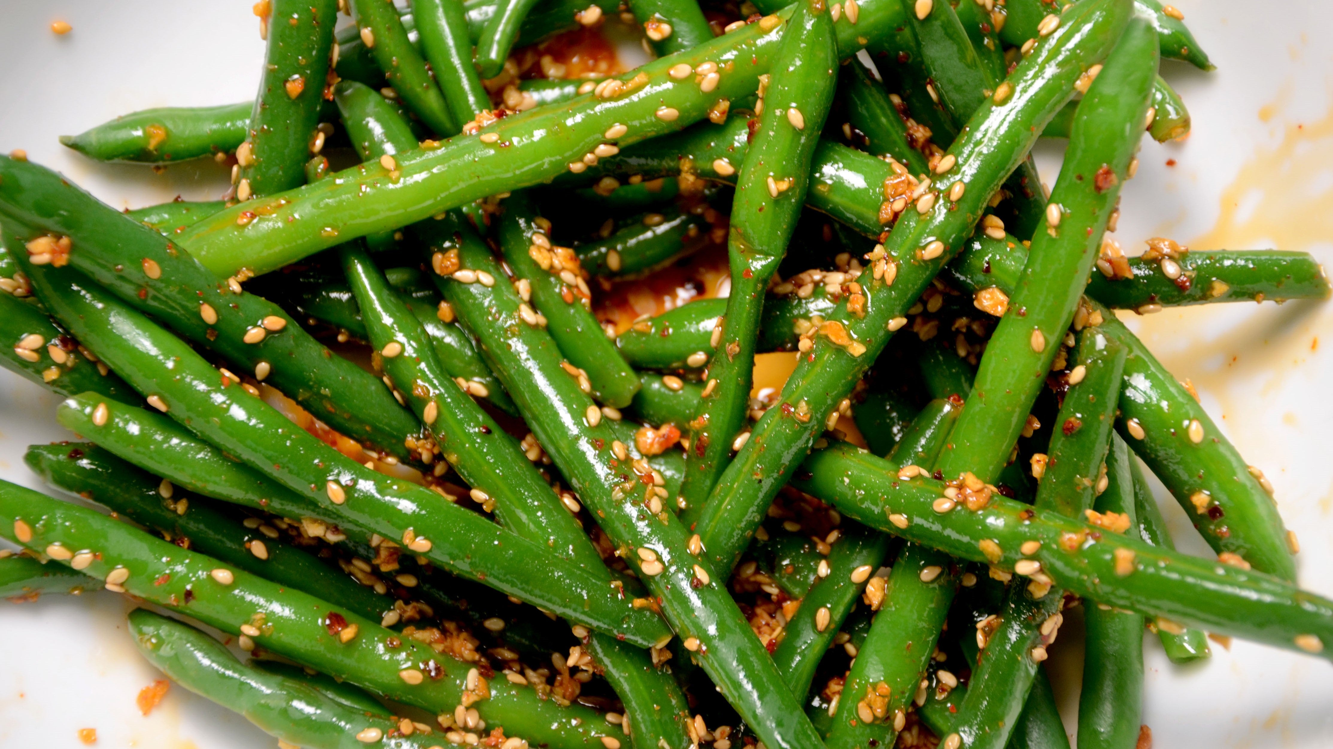 Steamed green beans lightly coated in Ruby Crunch chili crisp showing the crunchy toasted sesame seeds, garlic and spices clinging to the beans