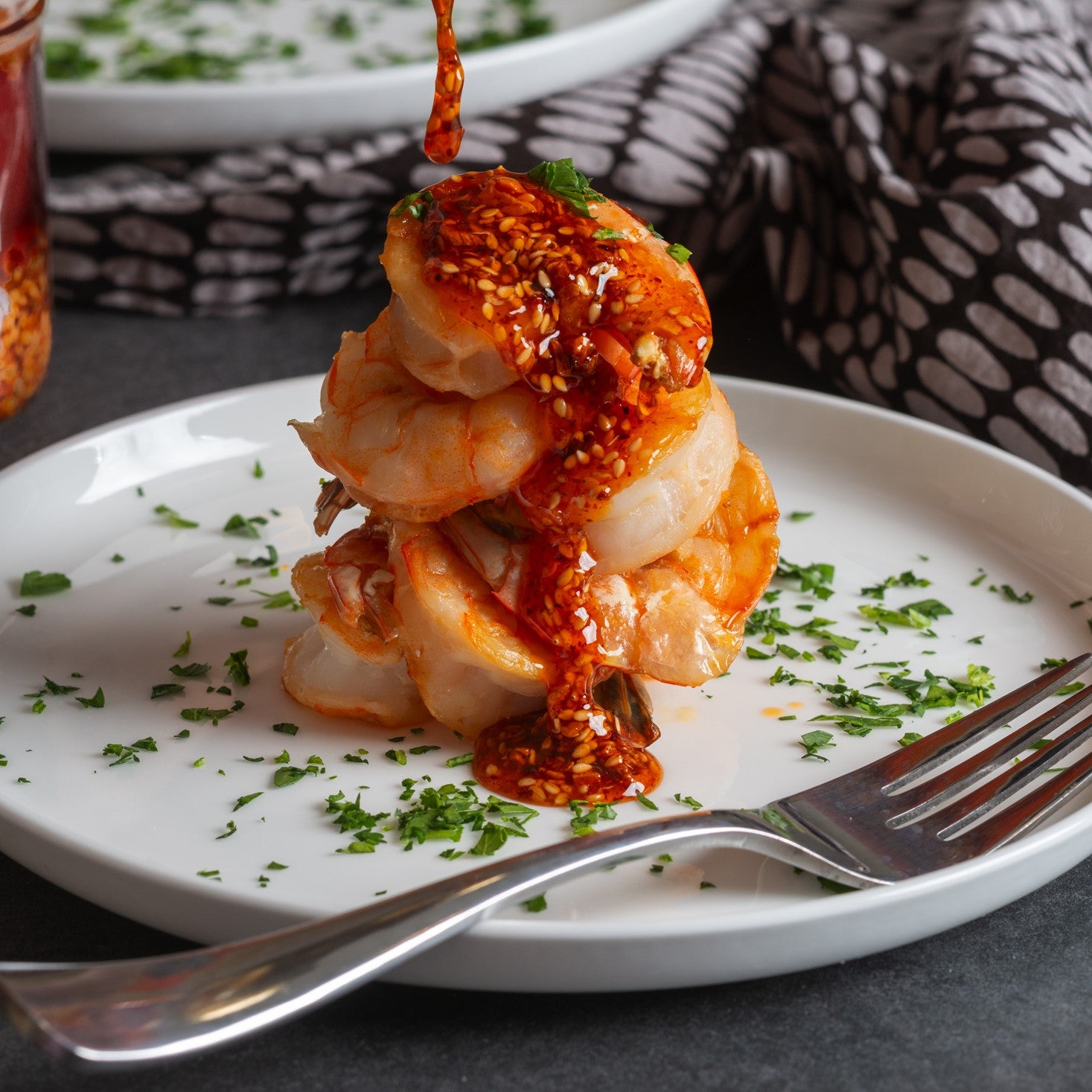 Ruby Crunch chili crisp drizzling onto stacked shrimp garnished with minced fresh parsley