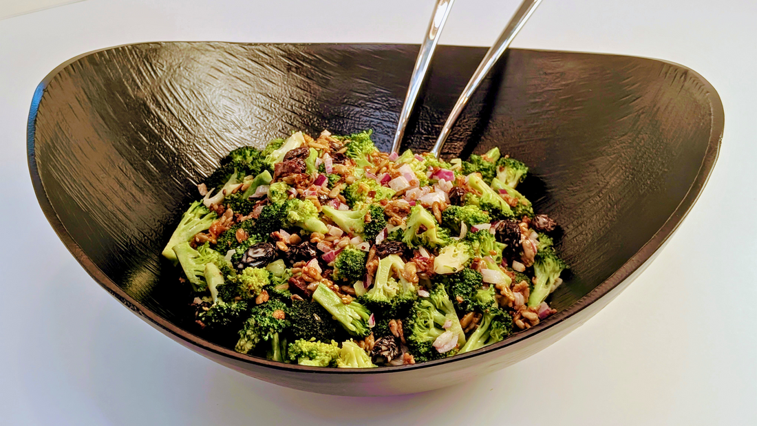 Black serving bowl with a salad of broccoli, bacon, raisins, red onion and crispy sunflower seeds toasted in Ruby Crunch chili crisp