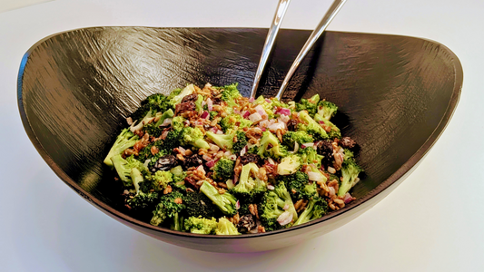 Black serving bowl with a salad of broccoli, bacon, raisins, red onion and crispy sunflower seeds toasted in Ruby Crunch chili crisp