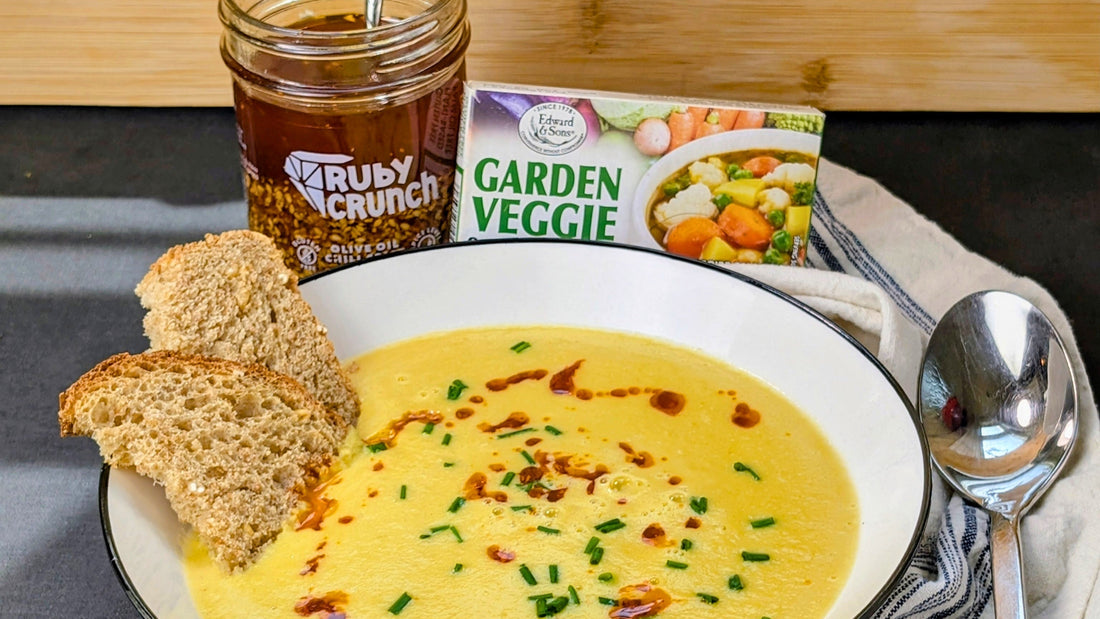 A bowl of creamy corn soup with rustic bread, a jar of Ruby Crunch and Edward & Sons bouillon.