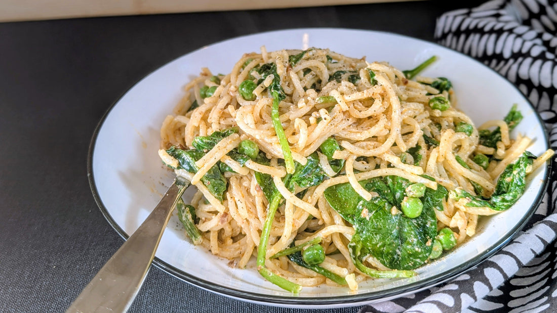 A bowl of spaghetti pasta with a light cream sauce, peas and spinach.