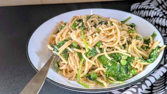 A bowl of spaghetti pasta with a light cream sauce, peas and spinach.