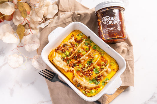 Baking dish with pot stickers nestled in eggs garnished with green onions and chili crisp with a jar of Ruby Crunch chili crisp